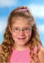 schoolfoto van Daphne, ze heeft lang golvend haar in een hoge staart en ze heeft een roze hemdje aan en een bril. 